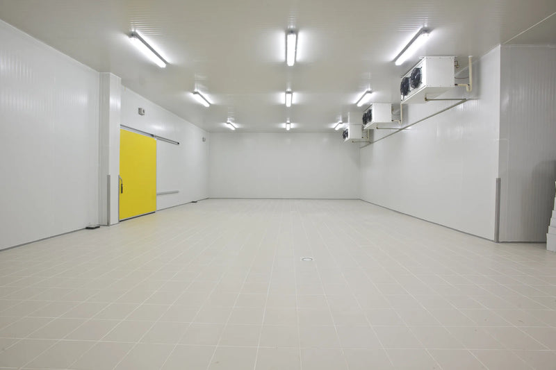 Large empty cold room with a yellow sliding door, tiled floor and wall-mounted evaporators