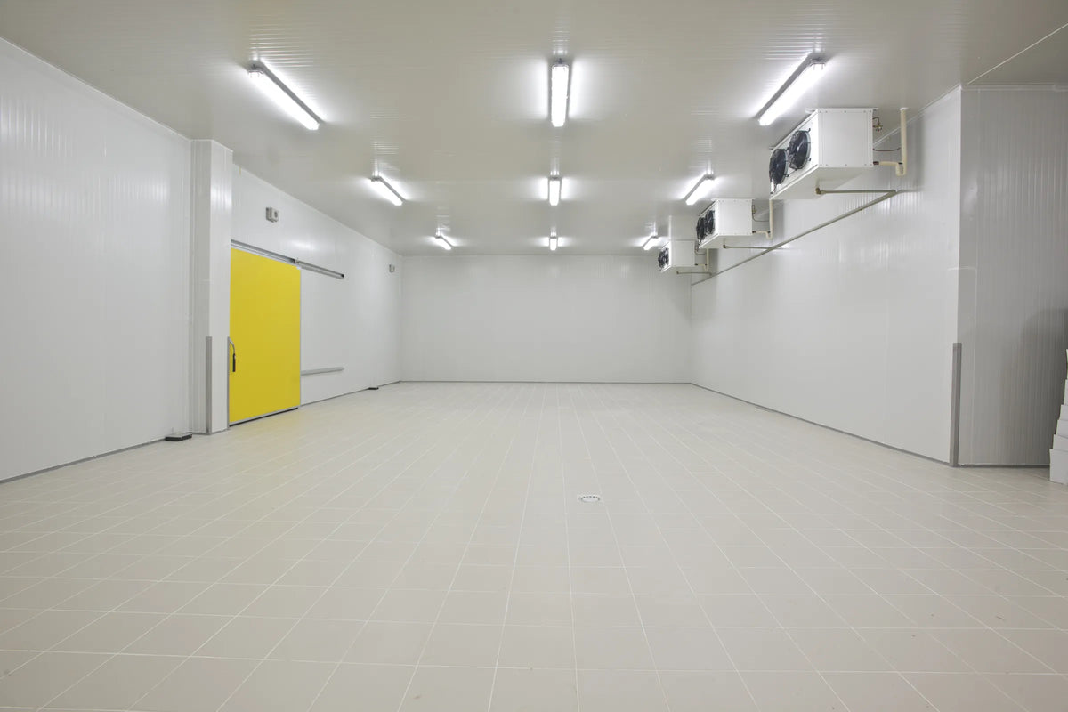 Large empty cold room with a yellow sliding door, tiled floor and wall-mounted evaporators