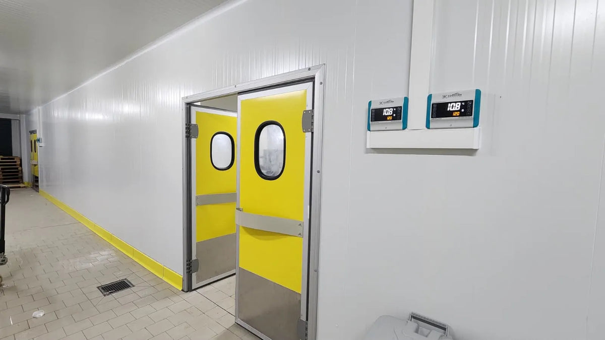 Corridor inside a cold store with yellow double swing doors and two digital temperature controllers on the wall