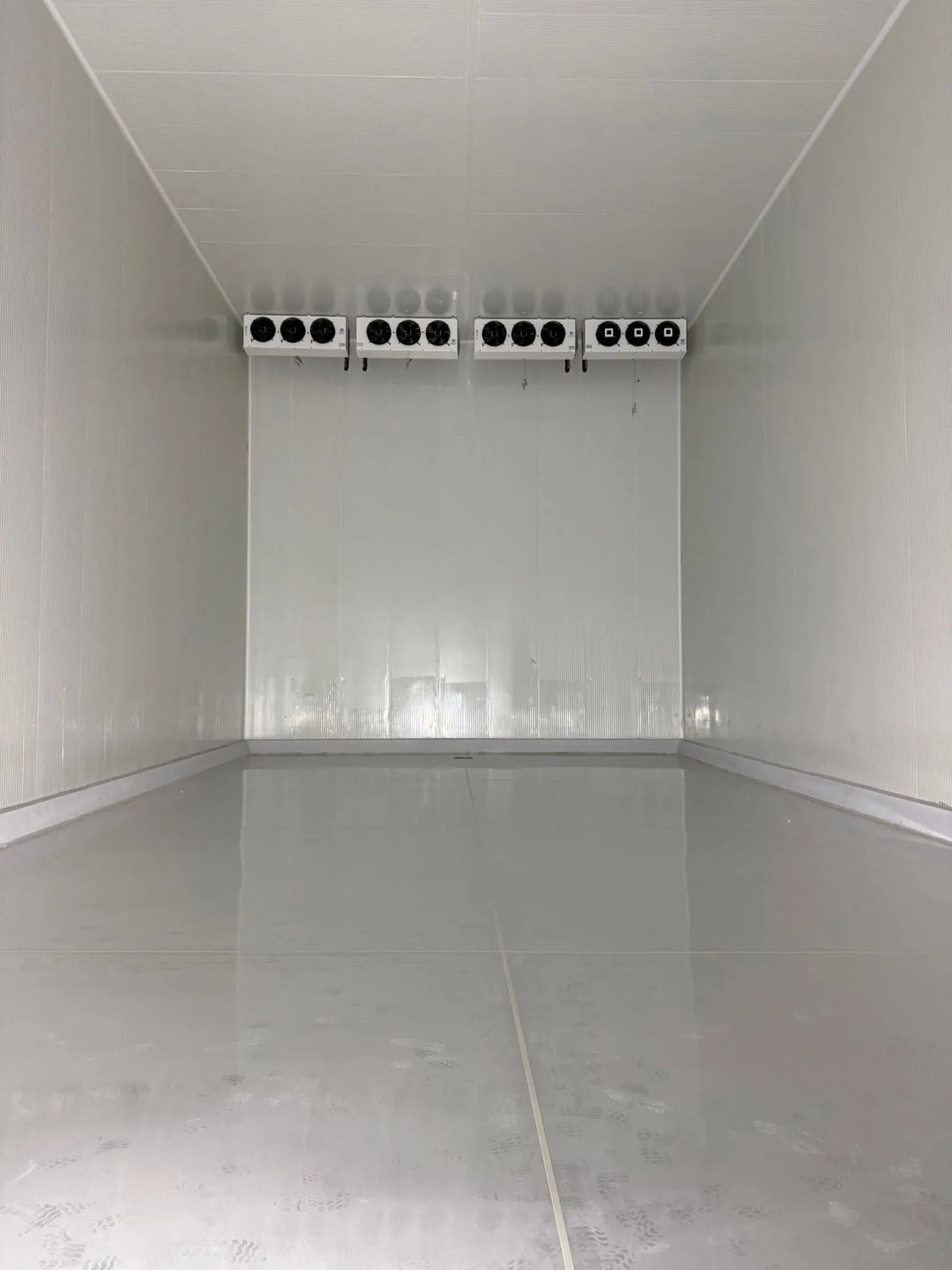 Empty walk-in freezer room with four evaporators on the back wall and a smooth insulated floor
